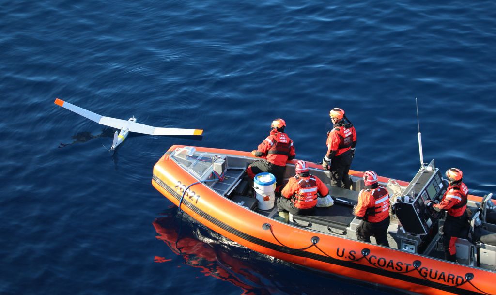 Coast Guard members in a boat pull a remote-controlled aircraft from the water.