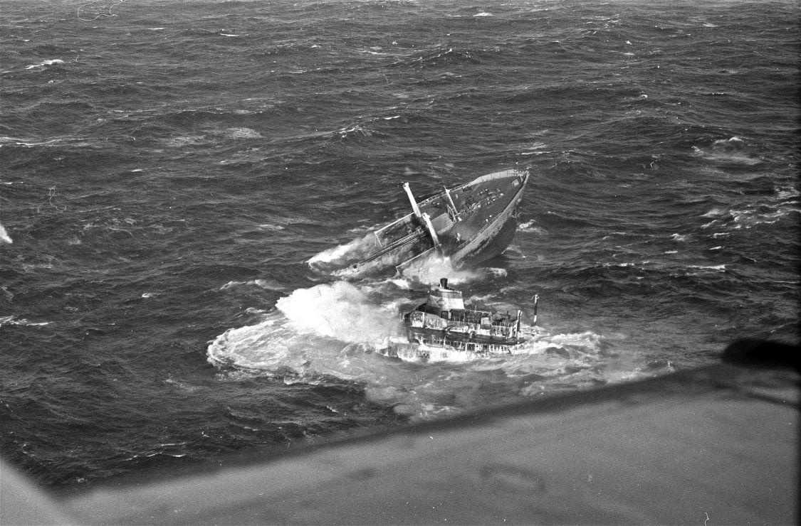 A sinking vessel's bow and stern have separated in high seas.