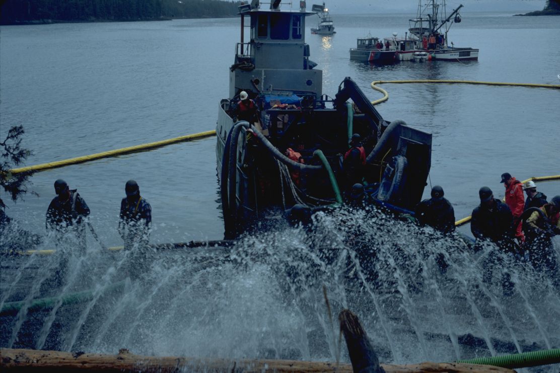 Photo of workers and a small ship spraying multiple streams of water.