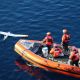 Coast Guard members in a boat pull a remote-controlled aircraft from the water.