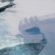 Shadows of people standing on a ship deck darken sea ice.