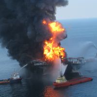 An explosion on an oil rig with several boats around it.