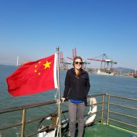 A woman next to a Chinese flag with water and an industrial shoreline in the background. 