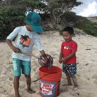 Two children putting debris into a bucket on a beach.