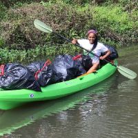 Woman paddling a kayak with bags of trash.