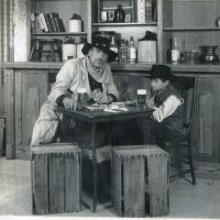 A black and white photo of a man and a child in old western clothes.