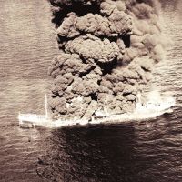 A black and white photo of smoke billowing from a sinking vessel.