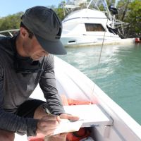 Man making written notes while sitting in a boat near a capsized boat.