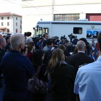 A group of people and press gather around a media vehicle.