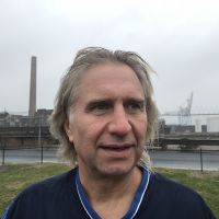 A profile shot of a man with an industrial setting in the background. 