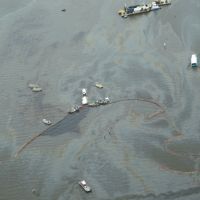 Overhead view of water with response vessels, boom and oily sheen.
