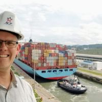 A man in a hard hat with a container ship in a canal lock behind him. 