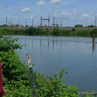 A person in a hard hat looking across a river at an industrial shoreline.
