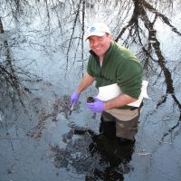 Image of a responder sampling water after an oil spill in Louisiana swamp.