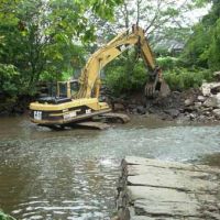 Excavator removes a rock dam from a stream.