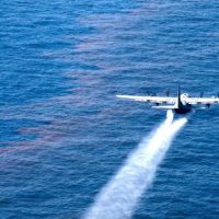 An Air Force plane drops an oil-dispersing chemical onto an oil slick on ocean.