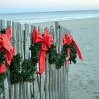Red bows and evergreen bows on a fence on a beach.