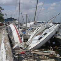 Wrecked sailboats and debris along a dock after a hurricane.