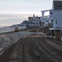 Machines moves sand to rebuild a New Jersey beach by Sandy-damaged houses.