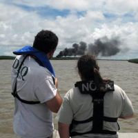 Two people observe smoke and burning in a marsh.