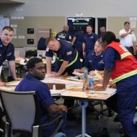 Group of Coast Guard members sit and stand at a table.
