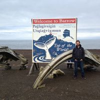 NOAA employee stands with bowhead whale bones and a welcome sign to Barrow.