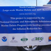 A sign highlighting the NOAA Marine Debris Program and North Carolina Coastal Federation's Large-Scale Marine Debris and Abandoned Derelict Vessel Removal project.