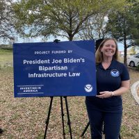 NOAA's Marine Debris Program Director Nancy Wallace holds sign stating support from the Bipartisan Infrastructure Law towards the installation project.
