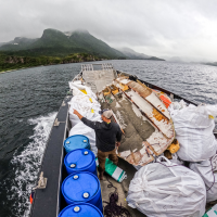 A person pointing to a mountainous shoreline while on a moving vessel that is full of various marine debris items.