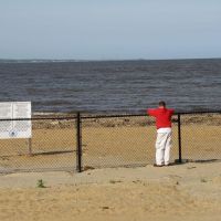 Laurence Harbor, New Jersey waterfront with an EPA public health hazard sign and a person in a red shirt and white pants standing behind a fence that restricts access to the beach.