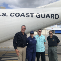 Four individuals supporting hurricane response pose for a group photo in front of an overflight plane.