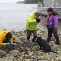 Three people on rocky shore with black dog. Image credit: NOAA.
