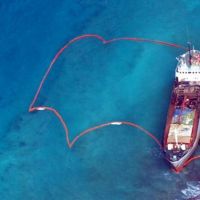 A ship run aground on coral reef, surrounded by protective oil boom.