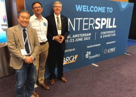 Three people pose for a photo next to a sign reading "Interspill."
