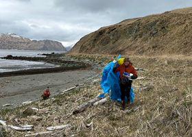 A photo of a participant carrying trash during a community marine debris cleanup in Humpy Cove, Unalaska, AK.
