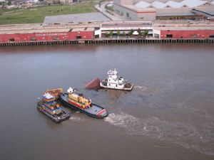 Three tugs work together to hold the damaged barge in place while black streamers of oil continue to release. Image Credit: USCG