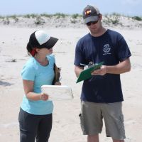 Two people on a beach looking at a clipboard.
