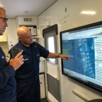 Two people in blue uniforms looking at a screen with a map on it.