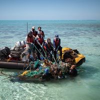 Group in a small boat hauling tangled nets and debris from the water. 