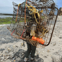 A person carrying derelict fishing gear across a beach.