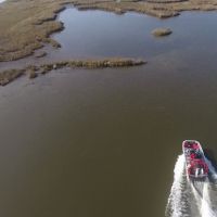 Aerial view of a boat heading towards a marsh.