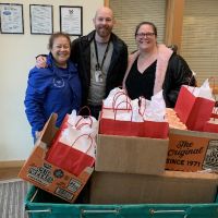 Three people posing with boxes of gift bags. 