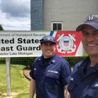 Two men looking into camera, USCG sign in background.