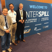 Three people pose for a photo next to a sign reading "Interspill."