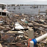 A vessel and a large pile of marine debris in the water next to a dock.