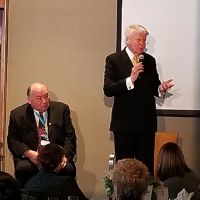 Two men at front of room addressing a group.