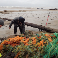 Two people on a beach hauling piles of fish netting.