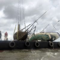 Sunken vessel being lifted from the water onto a boat.