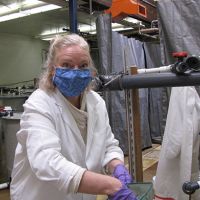 Woman in a mask and white coat working at a tank.