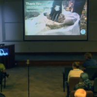 People in a dark classroom look at a presentation on a large screen